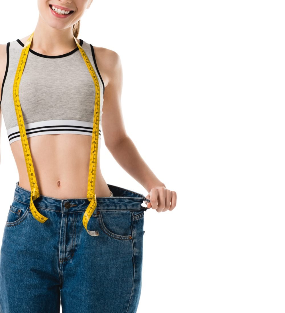 smiling slim woman with measuring tape in oversized jeans isolated on white